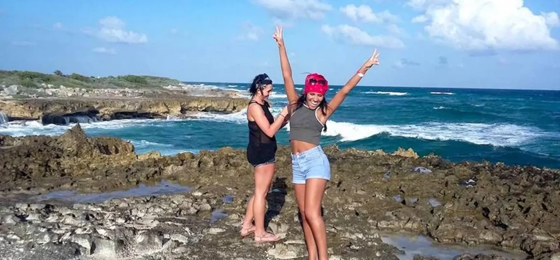 Two happy women celebrating on the rugged, rocky coastline of Cozumel's east side during an off-road adventure tour, with the blue ocean behind them.